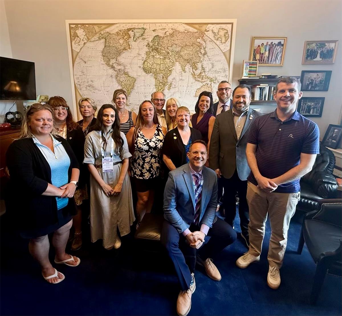 Group of people in an office setting with a blue carpet and world map on the wall behind them.